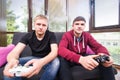 Two handsome young men playing video games while sitting on sofa Royalty Free Stock Photo