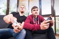 Two handsome young men playing video games while sitting on sofa Royalty Free Stock Photo