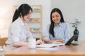 Two happy asian colleagues discussing new project, businesswomen using digital laptop together in office. Royalty Free Stock Photo