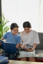 Two happy asian girl using tablet together and siting on sofa in living room. Royalty Free Stock Photo