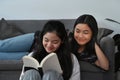 Two happy girls sitting in living room and reading book together. Royalty Free Stock Photo