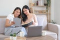 Two happy Asian women best friends in casual wear laughing while working with tablet at home in living room Royalty Free Stock Photo