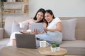 Two happy Asian women best friends in casual wear laughing while working with tablet at home in living room Royalty Free Stock Photo