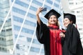 Two happy Asian young beautiful graduate female students with University degree standing and holding diploma taking selfie picture Royalty Free Stock Photo