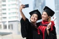 Two happy Asian young beautiful graduate female students with University degree standing and holding diploma taking selfie picture Royalty Free Stock Photo