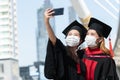 Two happy Asian young beautiful graduate female students wearing face mask standing and taking selfie picture with mobile phone Royalty Free Stock Photo