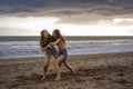 Two happy and attractive young Asian Chinese women girlfriends or sisters having fun playing wrestling on sunset beach in beautifu Royalty Free Stock Photo