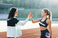 Two happy attractive young sportswomen giving high five after training. Sportswomen relaxing after jogging in park