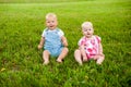 Two happy baby boy and a girl age 9 months old, sitting on the grass and interact, talk, look at each other. Royalty Free Stock Photo