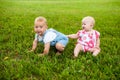 Two happy baby boy and a girl age 9 months old, sitting on the grass and interact, talk, look at each other. Royalty Free Stock Photo