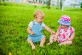 Two happy baby boy and a girl age 9 months old, sitting on the grass and interact, talk, look at each other. Royalty Free Stock Photo