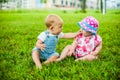 Two happy baby boy and a girl age 9 months old, sitting on the grass and interact, talk, look at each other. Royalty Free Stock Photo
