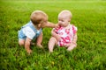 Two happy baby boy and a girl age 9 months old, sitting on the grass and interact, talk, look at each other. Royalty Free Stock Photo