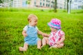 Two happy baby boy and a girl age 9 months old, sitting on the grass and interact, talk, look at each other. Royalty Free Stock Photo