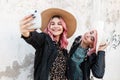 Two happy beautiful funny girls in fashionable denim clothes with a dress and hats take a selfie photo and enjoy a walk in the Royalty Free Stock Photo