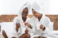 Happy black women in bathrobes drinking coffee, using smartphone