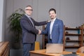 Two happy business partners in blue suits smiling and making handshake in office near the laptop Royalty Free Stock Photo