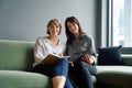 Two happy business women sitting on sofa using digital tablet during meeting in office Royalty Free Stock Photo