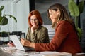 Two happy busy female coworkers working together using computer at desk in office. Royalty Free Stock Photo