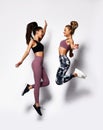 Two happy carefree young sport women jumping dancing laughing on white