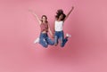 Two happy carefree young women jumping in the air with raised fists looking at camera isolated on pink background Royalty Free Stock Photo