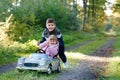 Two happy children playing with big old toy car in autumn forest, outdoors. Kid boy pushing and driving car with little Royalty Free Stock Photo