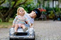 Two happy children playing with big old toy car in summer garden, outdoors. Kid boy driving car with little toddler girl Royalty Free Stock Photo