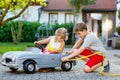 Two happy children playing with big old toy car in summer garden, outdoors. Kid boy refuel car with little toddler girl Royalty Free Stock Photo