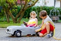 Two happy children playing with big old toy car in summer garden, outdoors. Kid boy refuel car with little toddler girl Royalty Free Stock Photo