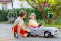 Two happy children playing with big old toy car in summer garden, outdoors. Kid boy refuel car with little toddler girl Royalty Free Stock Photo