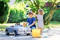 Two happy children washing big old toy car in summer garden, outdoors. Brother boy and little sister toddler girl Royalty Free Stock Photo