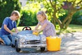 Two happy children washing big old toy car in summer garden, outdoors. Brother boy and little sister toddler girl Royalty Free Stock Photo