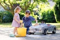 Two happy children washing big old toy car in summer garden, outdoors. Brother boy and little sister toddler girl Royalty Free Stock Photo