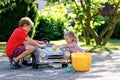 Two happy children washing big old toy car in summer garden, outdoors. Brother boy and little sister toddler girl Royalty Free Stock Photo