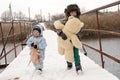 Two happy children in winter fashion clothes ride a sleigh with a toy pig and a bear on a bridge across the river. First snow, fam Royalty Free Stock Photo