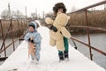 Two happy children in winter fashion clothes ride a sleigh with a toy pig and a bear on a bridge across the river. First snow, fam Royalty Free Stock Photo