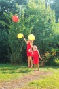 Two happy cute little sisters jumping with colorful toy balloons outdoors. Smiling kids having fun in green spring garden at warm Royalty Free Stock Photo