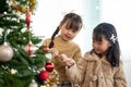Two happy and cute young Asian girls in cute dresses are having fun and decorating a Christmas tree Royalty Free Stock Photo