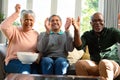 Two happy diverse senior couple and their african american male friend watching tv and having fun