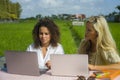 Two happy female friends working outdoors at beautiful internet cafe with laptop computer caucasian woman and an afro mixed girl Royalty Free Stock Photo