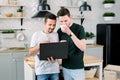 Two happy friends having fun while using laptop together. Happy smiling gay couple using laptop at the kitchen at home Royalty Free Stock Photo