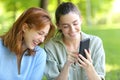 Two happy friends laughing checking phone in a park Royalty Free Stock Photo