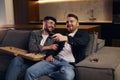 Two happy gay men are watching TV while holding each other`s hand Royalty Free Stock Photo