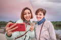 Happy girl friends taking selfie photographs on mobile phones with bright rainbow stretches over the river Royalty Free Stock Photo