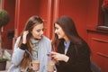 Two happy girl friends talking and drinking coffee in autumn city in cafe. Meeting of good friends, young fashionable students
