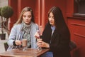 Two happy girl friends talking and drinking coffee in autumn city in cafe. Meeting of good friends, young fashionable students