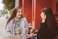 Two happy girl friends talking and drinking coffee in autumn city in cafe. Meeting of good friends, young fashionable students Royalty Free Stock Photo