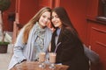 Two happy girl friends talking and drinking coffee in autumn city in cafe. Meeting of good friends, young fashionable students