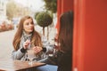 Two happy girl friends talking and drinking coffee in autumn city in cafe. Meeting of good friends, young fashionable students