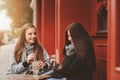 Two happy girl friends talking and drinking coffee in autumn city in cafe. Meeting of good friends, young fashionable students